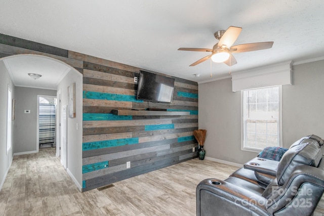 living room with crown molding, a wealth of natural light, light wood-type flooring, and wood walls