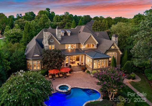 back house at dusk with a patio and an in ground hot tub