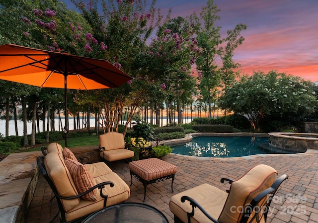 pool at dusk featuring an in ground hot tub, a water view, an outdoor hangout area, and a patio