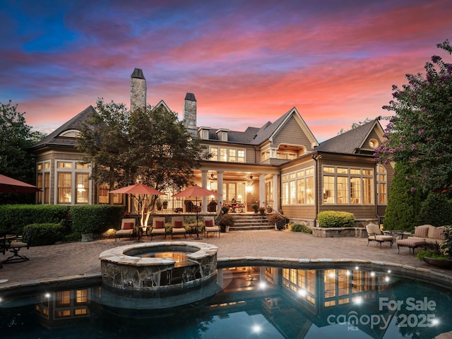 pool at dusk with an in ground hot tub and a patio