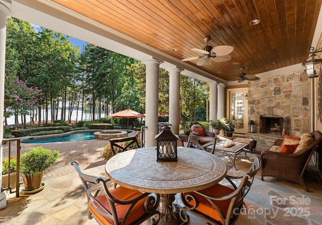 view of patio / terrace with a fenced in pool, a water view, an outdoor stone fireplace, and ceiling fan