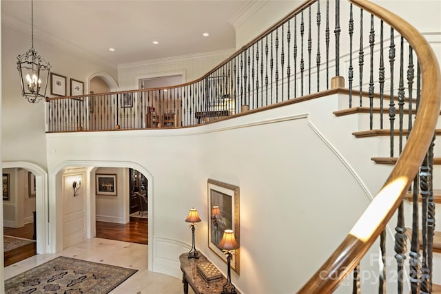 stairway with a towering ceiling, ornamental molding, and a notable chandelier