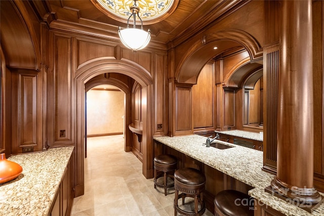 bar featuring sink, pendant lighting, light stone counters, and wood walls