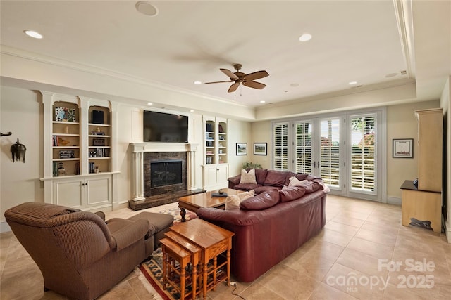 living room with a raised ceiling, a premium fireplace, ceiling fan, and built in shelves