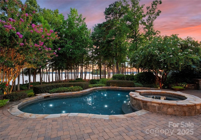 pool at dusk featuring an in ground hot tub and a water view