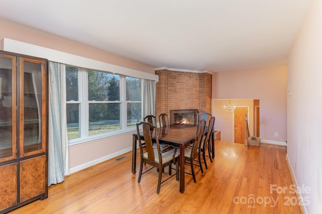 dining room with an inviting chandelier, a fireplace, and light hardwood / wood-style floors