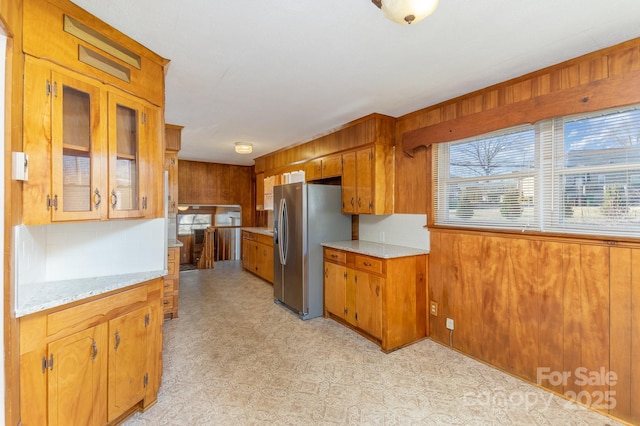 kitchen with stainless steel fridge with ice dispenser, wooden walls, and light stone countertops