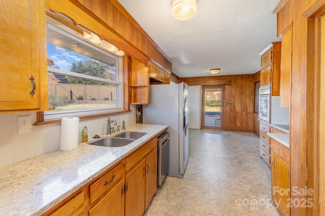 kitchen featuring wooden walls, dishwasher, sink, decorative backsplash, and light stone counters