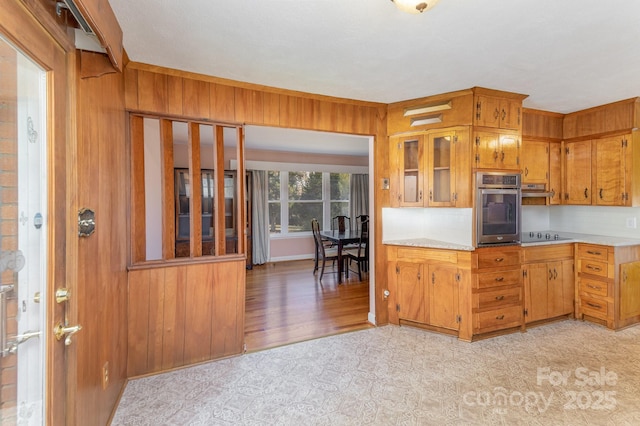 kitchen with black electric cooktop, oven, and wood walls