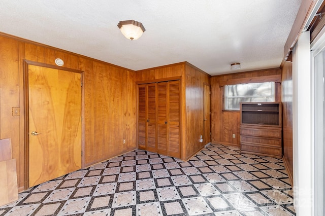 unfurnished bedroom featuring wood walls, a textured ceiling, and a closet