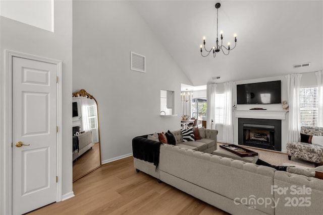 living room with an inviting chandelier, a healthy amount of sunlight, high vaulted ceiling, and light hardwood / wood-style flooring