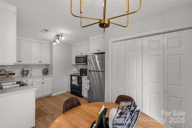 kitchen featuring sink, white cabinetry, tasteful backsplash, appliances with stainless steel finishes, and light hardwood / wood-style floors