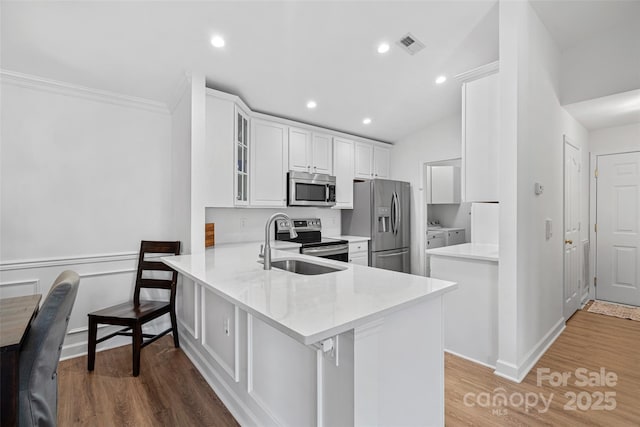 kitchen featuring a breakfast bar area, stainless steel appliances, wood-type flooring, white cabinets, and kitchen peninsula