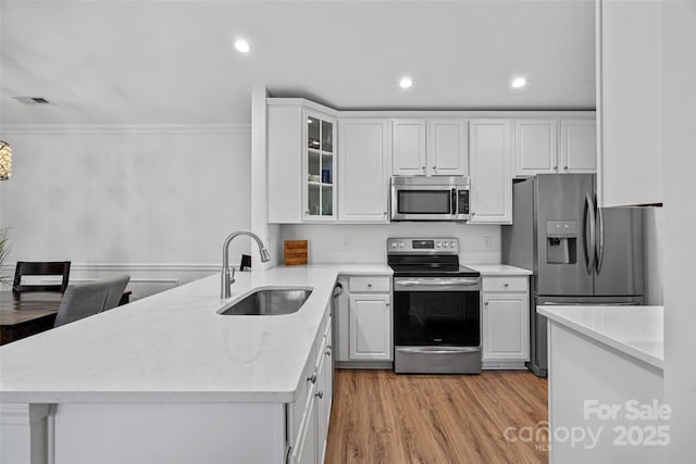 kitchen featuring appliances with stainless steel finishes, sink, white cabinets, ornamental molding, and light hardwood / wood-style flooring