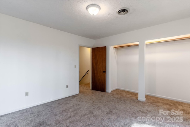 unfurnished bedroom featuring multiple closets, light carpet, and a textured ceiling