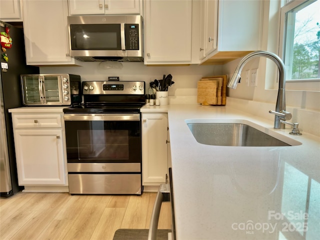 kitchen with light wood-type flooring, stainless steel appliances, sink, and white cabinets