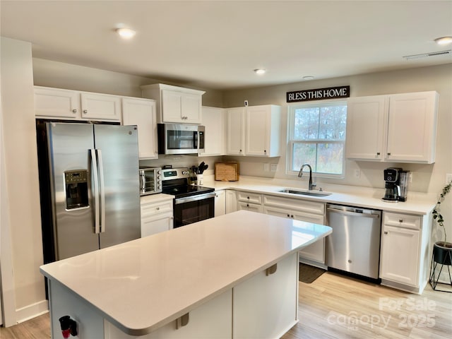 kitchen featuring sink, appliances with stainless steel finishes, white cabinets, a kitchen island, and light wood-type flooring