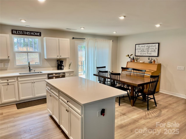 kitchen with sink, white cabinetry, a center island, light hardwood / wood-style floors, and stainless steel dishwasher