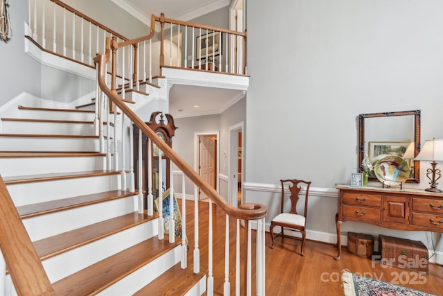 staircase featuring crown molding, a towering ceiling, and hardwood / wood-style flooring