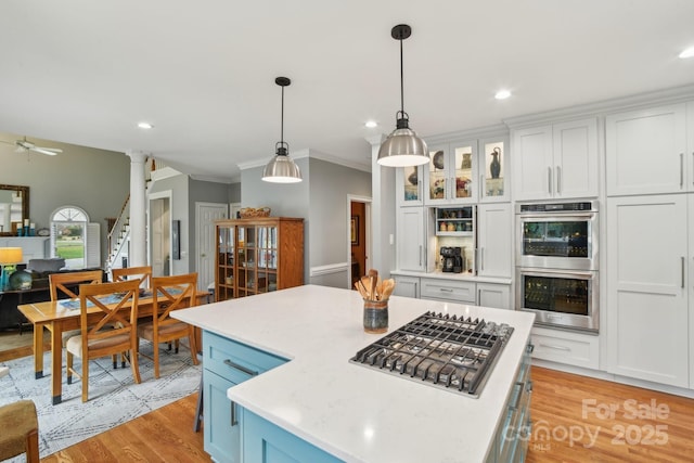 kitchen with stainless steel appliances, white cabinets, a kitchen island, decorative light fixtures, and light wood-type flooring