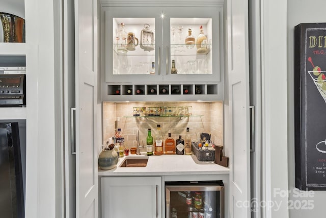 bar with beverage cooler, sink, decorative backsplash, and white cabinets