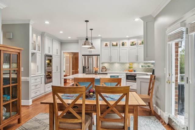 kitchen with pendant lighting, backsplash, stainless steel appliances, ornamental molding, and white cabinets