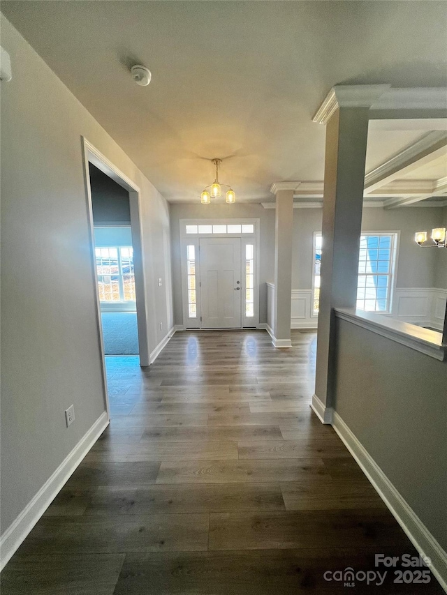 foyer entrance featuring dark wood-style floors, baseboards, decorative columns, and an inviting chandelier