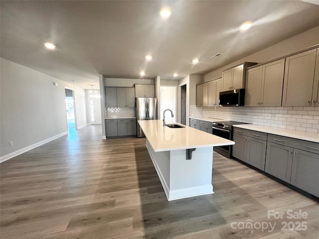 kitchen featuring a center island with sink, stainless steel appliances, light countertops, gray cabinetry, and a sink