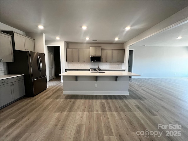 kitchen featuring gray cabinetry, light countertops, a sink, and an island with sink