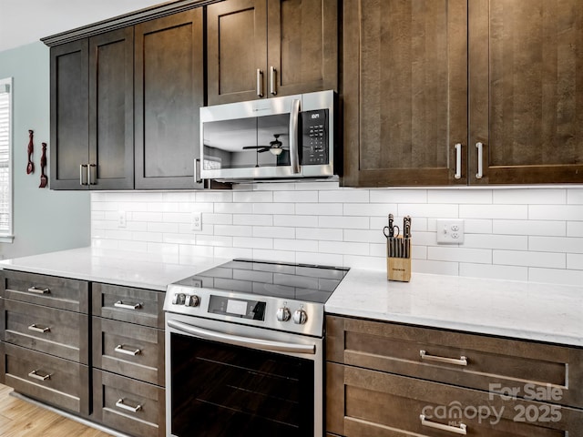 kitchen featuring light stone counters, stainless steel appliances, decorative backsplash, dark brown cabinets, and light wood-type flooring