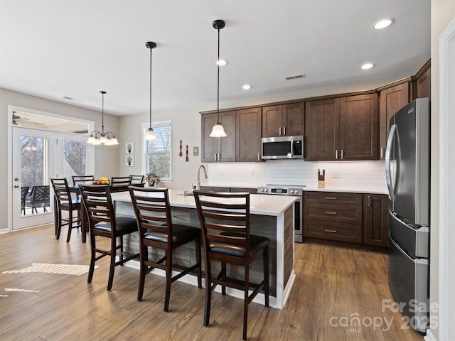 kitchen with wood finished floors, visible vents, dark brown cabinetry, appliances with stainless steel finishes, and tasteful backsplash