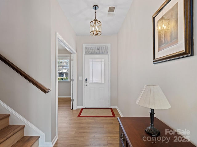 entryway with visible vents, a notable chandelier, wood finished floors, baseboards, and stairs