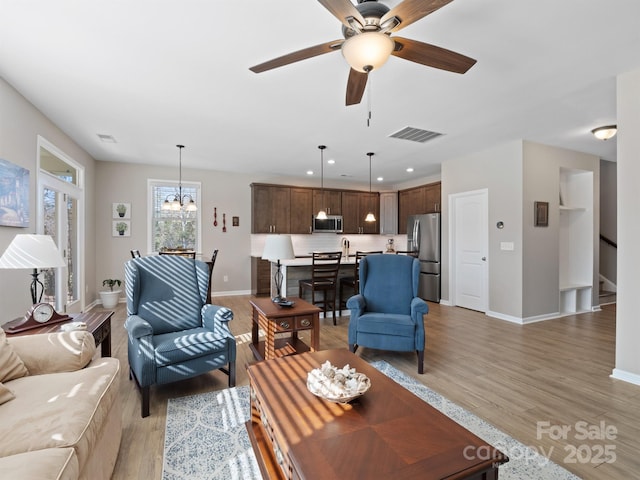 living area with light wood finished floors, visible vents, baseboards, recessed lighting, and ceiling fan with notable chandelier