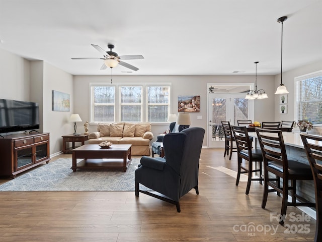 living area with ceiling fan with notable chandelier, baseboards, and wood finished floors