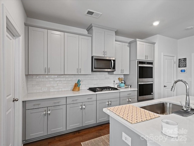 kitchen featuring sink, dark wood-type flooring, appliances with stainless steel finishes, gray cabinetry, and backsplash