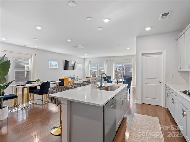 kitchen with sink, white cabinetry, light wood-type flooring, stainless steel dishwasher, and a kitchen island with sink