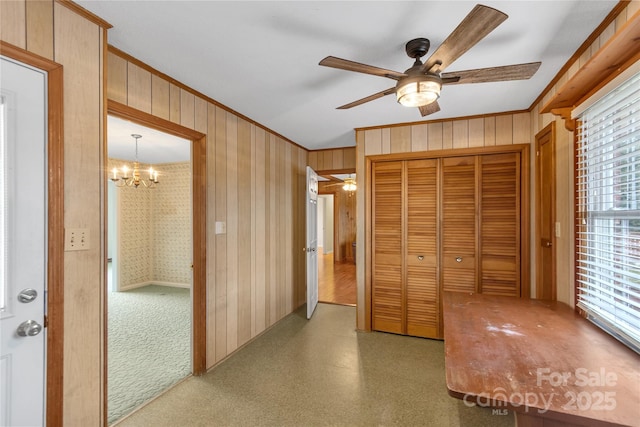 hall with crown molding, wooden walls, and a chandelier