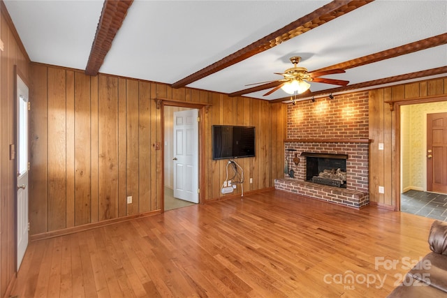 unfurnished living room featuring hardwood / wood-style flooring, ceiling fan, a fireplace, and beamed ceiling