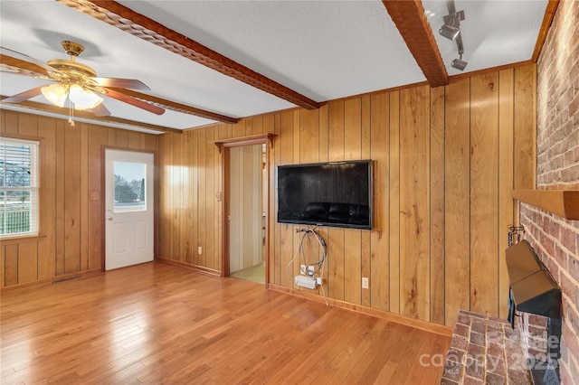 unfurnished living room featuring wood-type flooring, ceiling fan, a fireplace, and beam ceiling