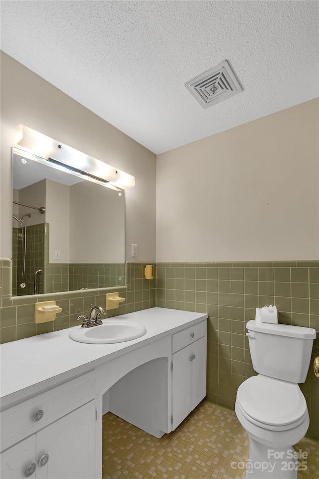 bathroom with tile walls, vanity, a tile shower, a textured ceiling, and toilet