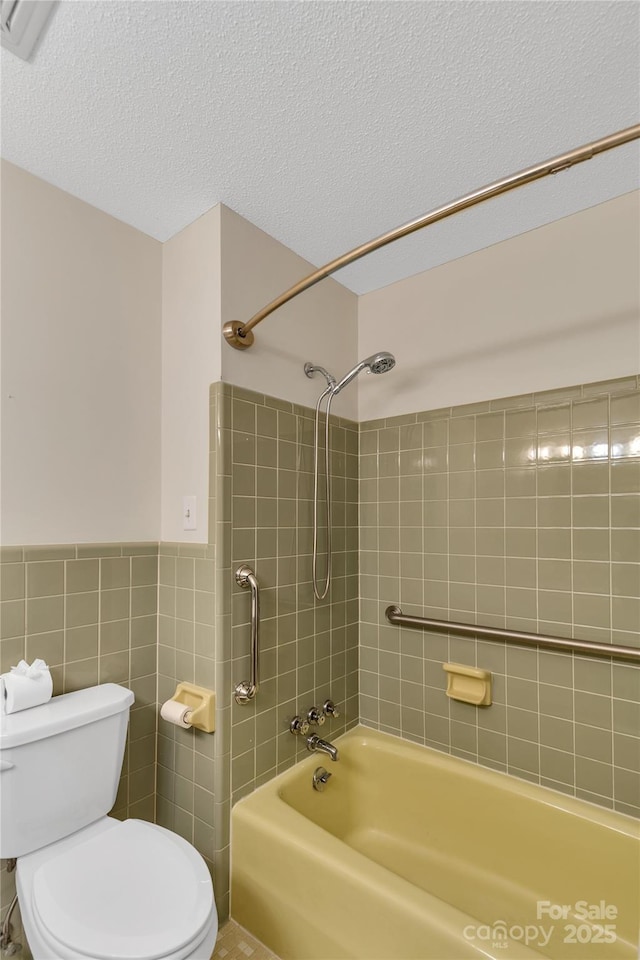 bathroom with tiled shower / bath, toilet, a textured ceiling, and tile walls