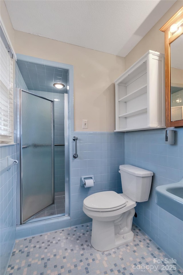 bathroom featuring tile walls, toilet, a shower with door, tile patterned floors, and a textured ceiling