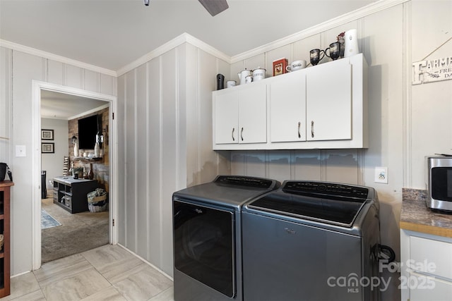 clothes washing area with crown molding, cabinets, and washer and dryer