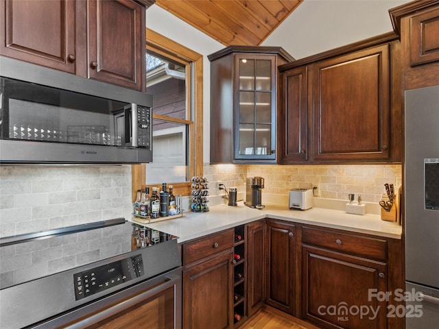 kitchen featuring lofted ceiling, decorative backsplash, dark brown cabinetry, and appliances with stainless steel finishes