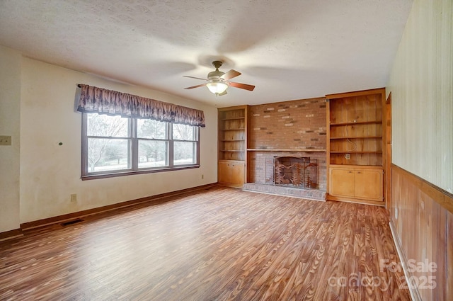 unfurnished living room with built in shelves, a fireplace, a textured ceiling, and hardwood / wood-style flooring