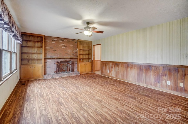 unfurnished living room with hardwood / wood-style floors, ceiling fan, a brick fireplace, a textured ceiling, and built in shelves