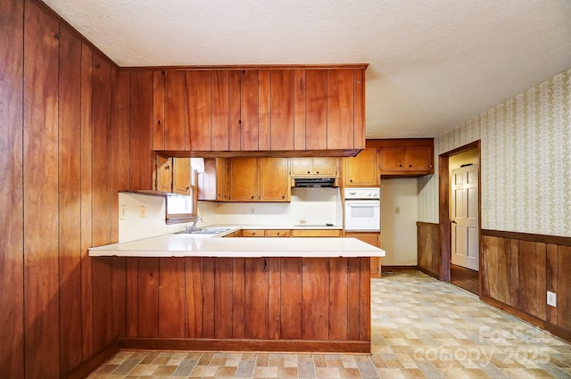 kitchen with sink, kitchen peninsula, oven, and wood walls