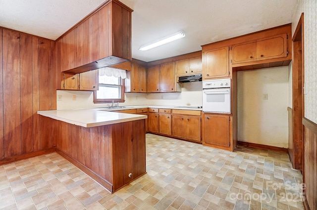 kitchen with wood walls, kitchen peninsula, white oven, and black cooktop