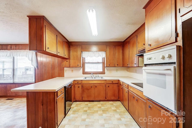 kitchen featuring sink, dishwasher, white oven, kitchen peninsula, and wood walls