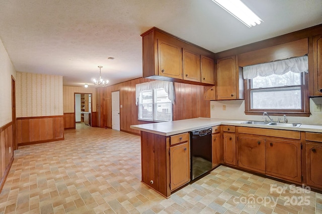 kitchen featuring sink, wood walls, black dishwasher, kitchen peninsula, and pendant lighting